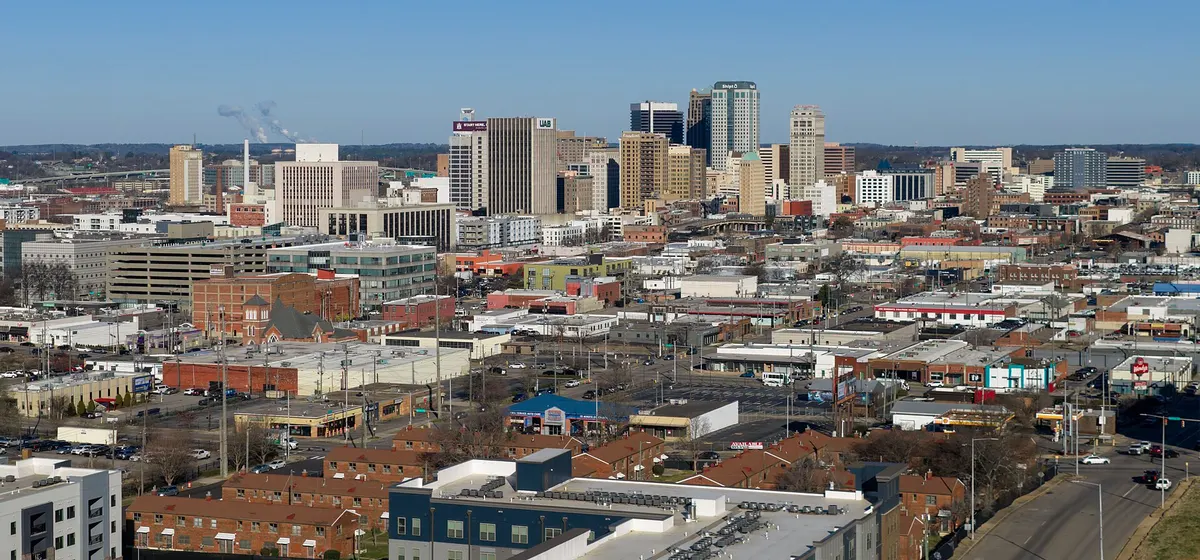 Downtown Birmingham's office towers rising above low brick buildings and streets under a clear blue sky