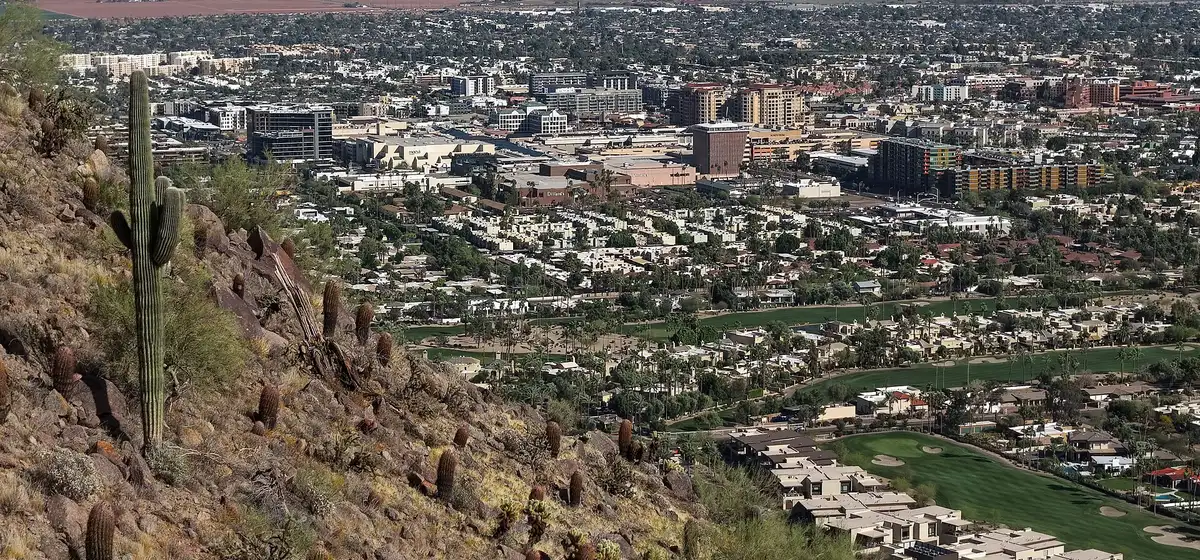 Downtown Scottsdale spread across the desert floor, seen from the rocky slope of Camelback Mountain with a saguaro cactus in front
