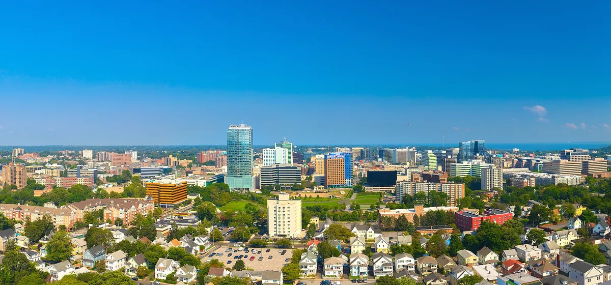 Downtown Stamford's office towers rising beyond streets of houses and trees on a clear summer day