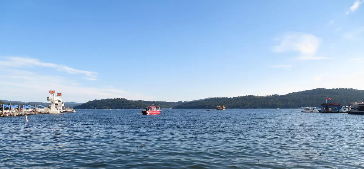 Open water of Lake Coeur d'Alene with a boat and wooded hills along the far shore