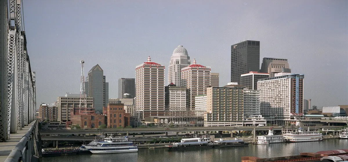 Downtown Louisville's towers above the Ohio River waterfront, with a towboat pushing barges in front