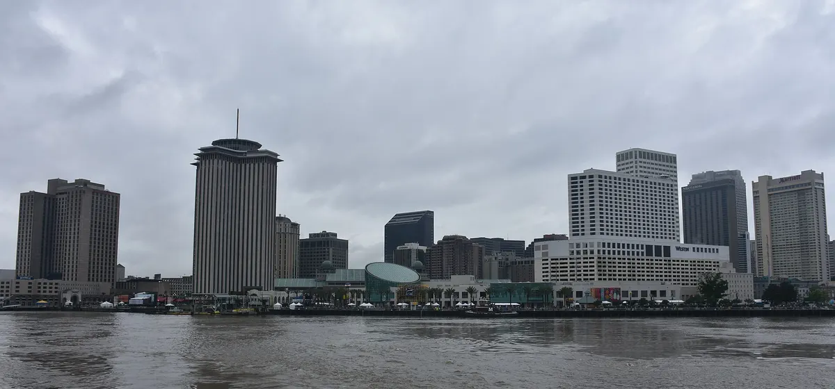 Downtown New Orleans' towers seen across the brown water of the Mississippi River under a grey sky