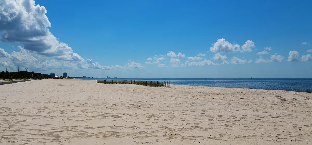 A wide, empty sand beach on the Gulf of Mexico near Gulfport under a blue sky with scattered clouds