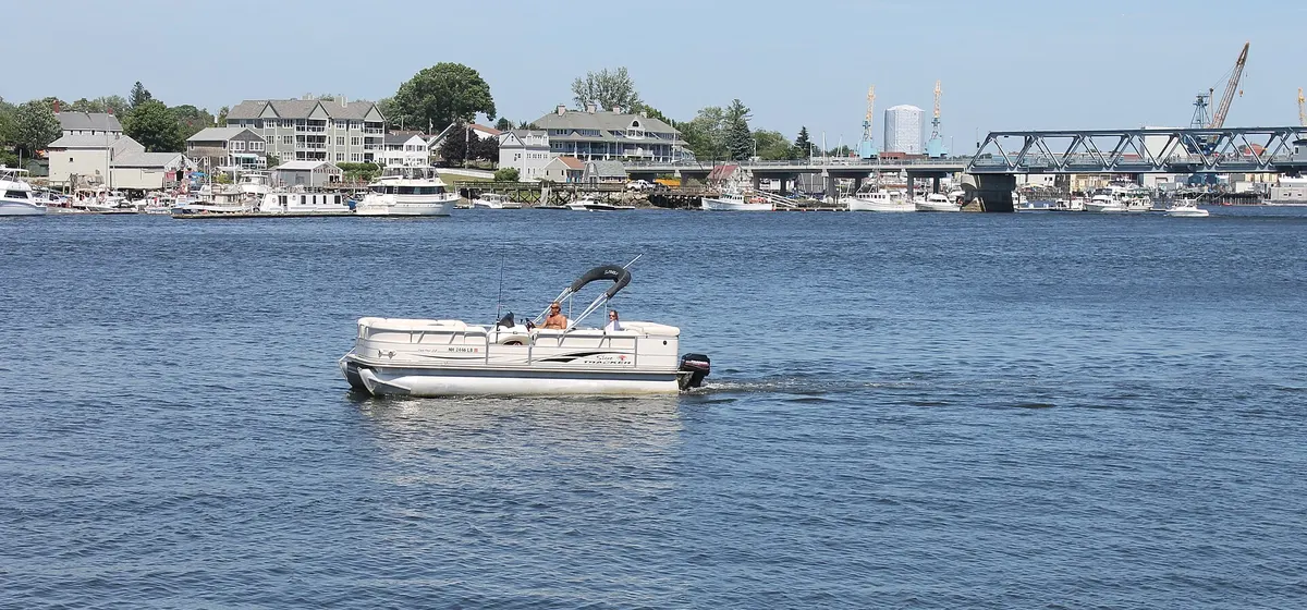 A pontoon boat on the river at Portsmouth, with waterfront houses and a steel bridge behind