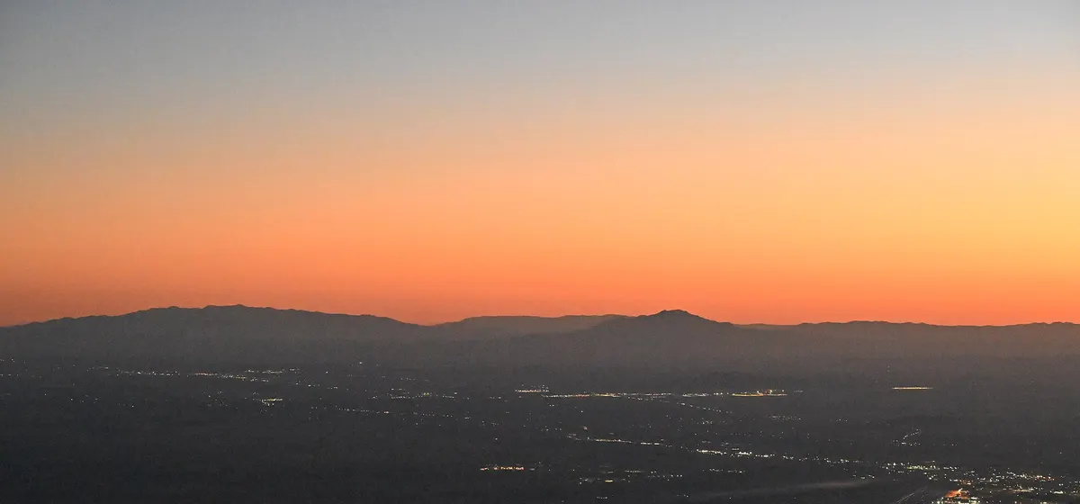 The lights of Albuquerque spread across the valley at dusk, seen from Sandia Peak, with mountains against an orange sky