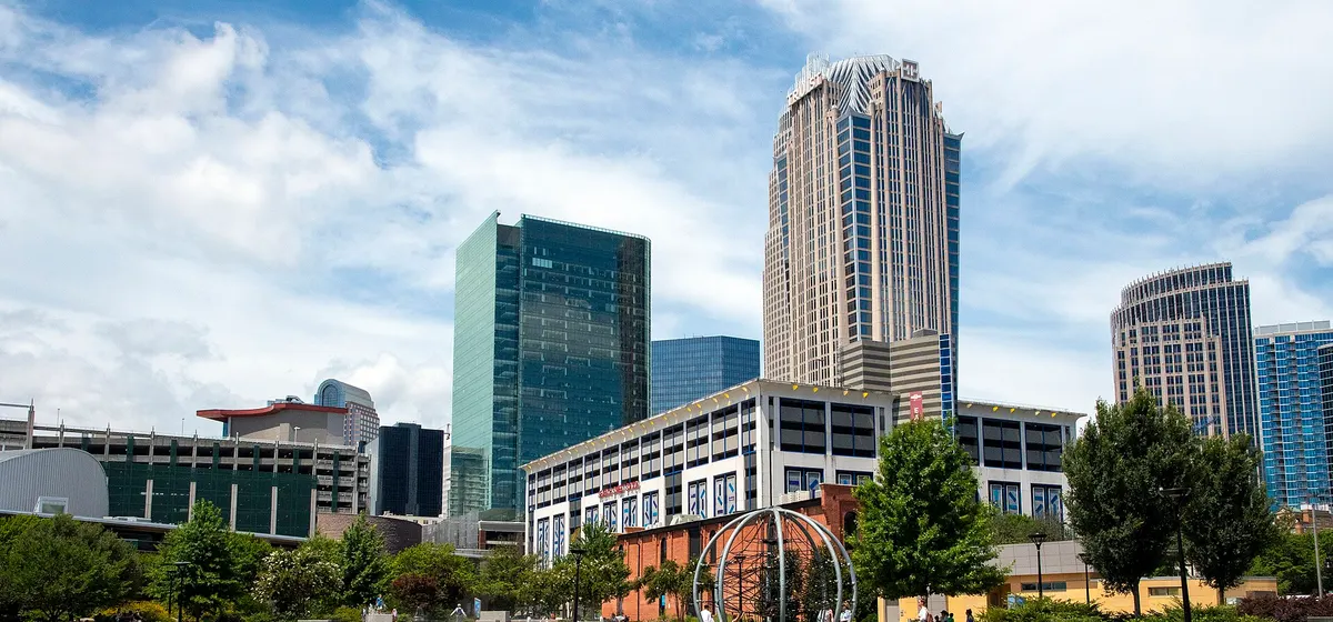 Uptown Charlotte's glass office towers above a green park lawn and a curving walkway on a partly cloudy day