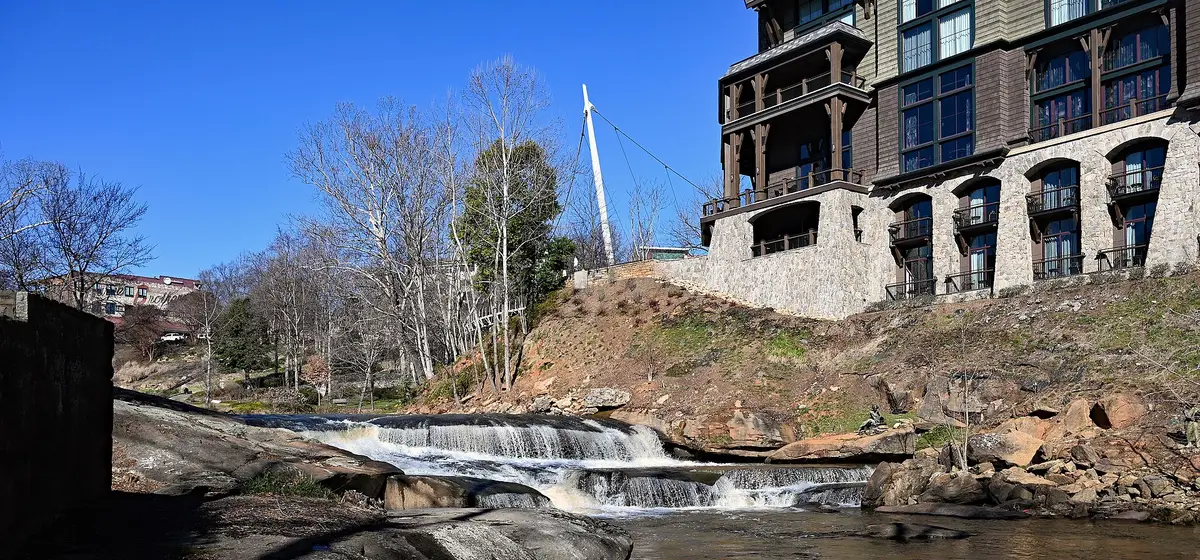 The Reedy River tumbling over rock ledges in Falls Park, with downtown Greenville buildings on the bank above