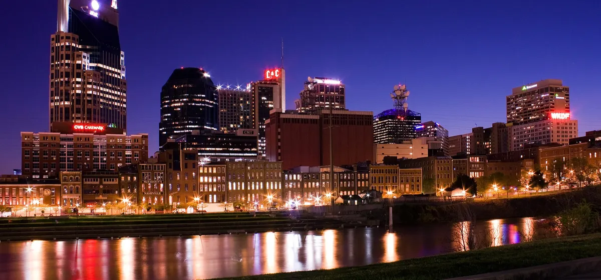 Downtown Nashville lit up at night, its towers reflected in the Cumberland River