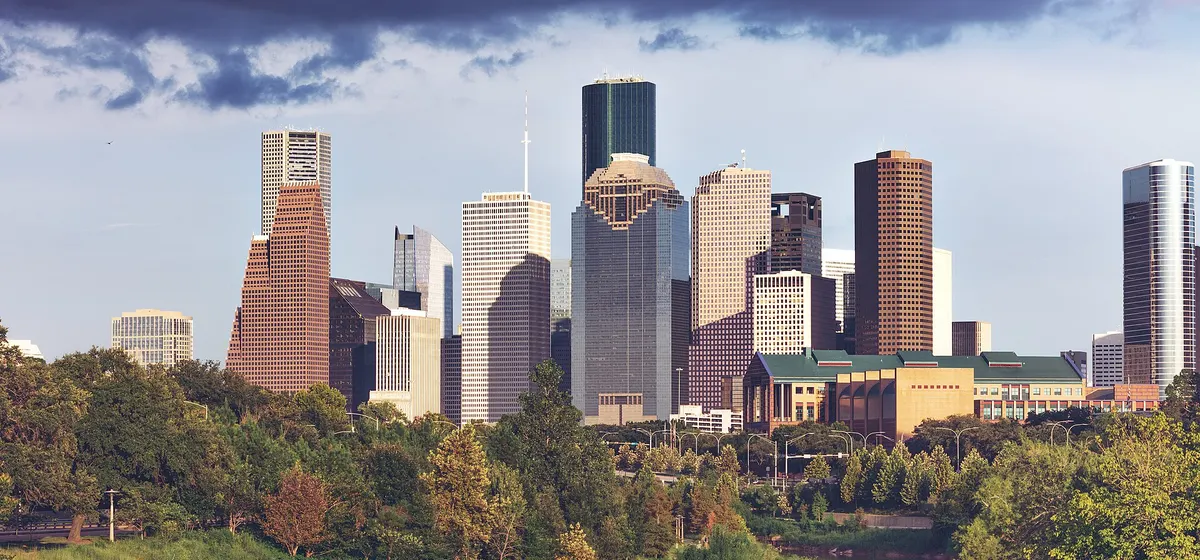 Downtown Houston's towers rising above the trees along Buffalo Bayou under a stormy sky